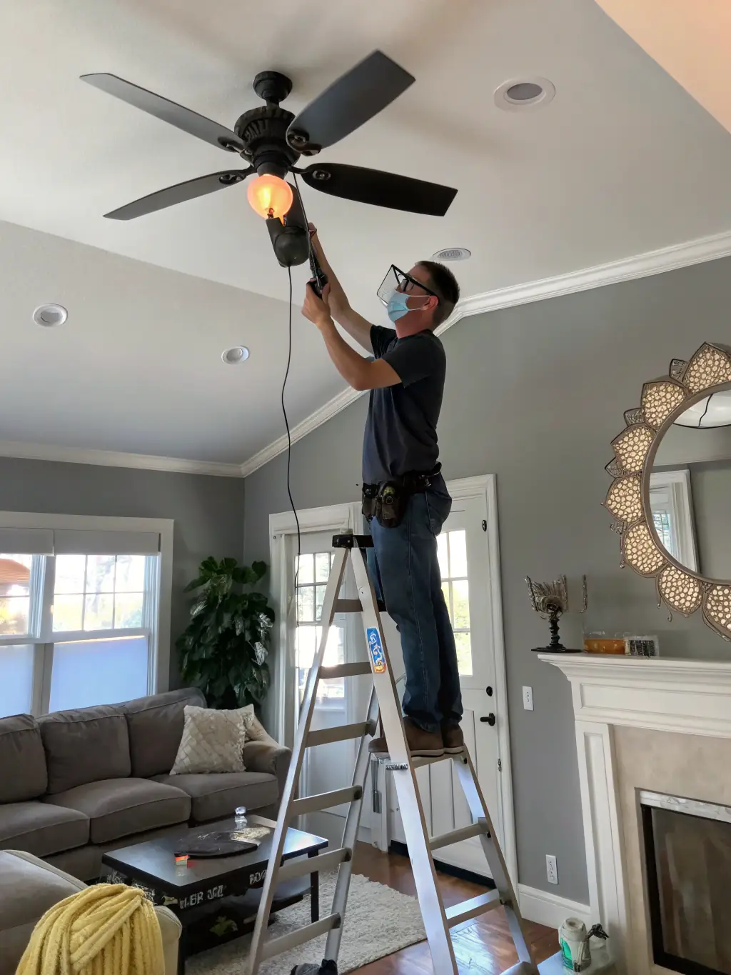 An electrician installing a new ceiling fan in a modern living room, showcasing Bright Home Crew's electrical services.