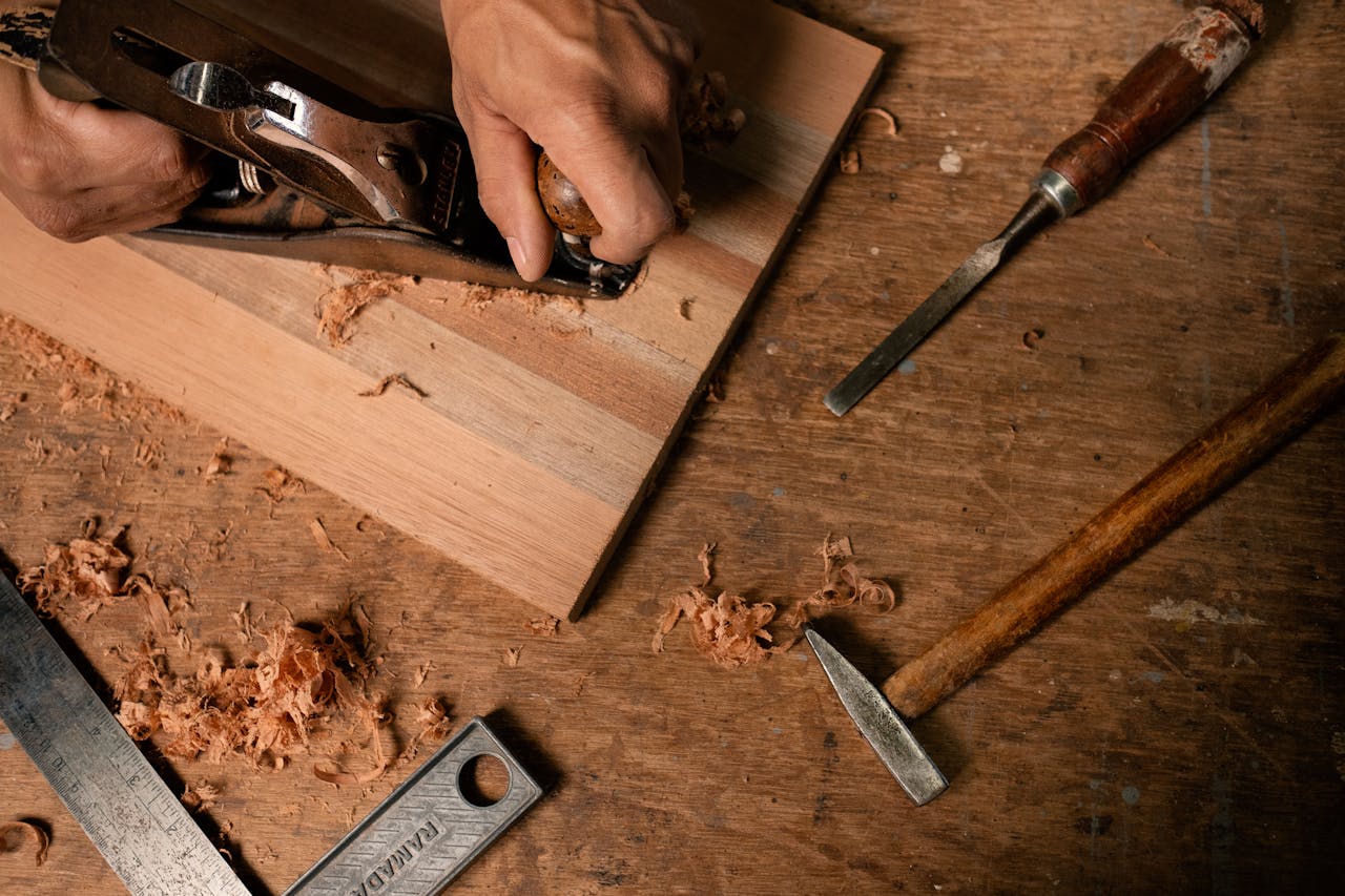 Close-up of hands using a planer on wood with tools and shavings around.